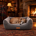 A Whippet asleep in the Balmoral grey herringbone bolster bed by Ralph & Co, by a fire in a Highland lodge library