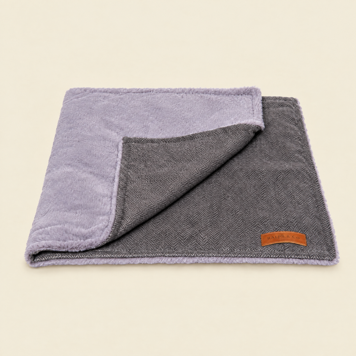 The Balmoral Grey Herringbone & Faux Fur Reversible Blanket by Ralph & Co, folded, on a cream background