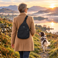 Woman on a Lake District lakeside path at sunrise wearing the black PupClub sling bag, Springer Spaniel ahead