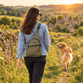 Woman walking a Cotswold footpath wearing the khaki green PupClub sling bag, Golden Retriever trotting ahead